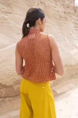 Top tejido color beige con espalda calada y cuello mao. Presenta cierre frontal con cordones y detalle de broches decorativos en el cuello.