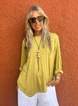 Buzo oversize color mostaza, con cuello redondo y mangas largas con puños anchos. Presenta un corte desigual en la base.