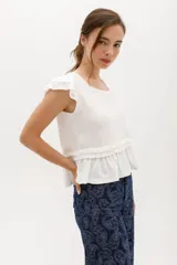 Remera color beige con cuello redondo, mangas cortas con volados y frunce con volados en la cintura.