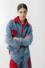 Campera de jean celeste con detalles de crochet rojo en cuello, bolsillo y ruedo. Tiene cierre frontal con botones dorados, bolsillos laterales y corte holgado.