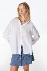 Camisa de lino color blanco, de manga larga y corte holgado, con cuello camisero y cierre frontal de botones.