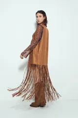 Chaleco largo color beige claro, estilo chaleco de gamuza, con apliques metálicos circulares perforados y largos flecos en el ruedo.