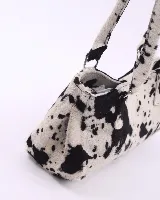 Cartera baguette de cuero con estampado animal print de vaca en tonos marrón y blanco. Tiene forro interior, un bolsillo amplio y broches laterales para ajustar el tamaño.