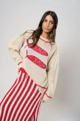 Sweater tejido color crudo con cuello redondo y mangas largas. Presenta dos peces rojos con detalles en azul bordados en el frente. Tiene ribete ondulado rojo en cuello, puños y ruedo.