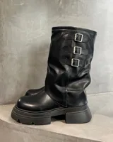 Botas negras de caña media con suela track, punta redonda y tres hebillas decorativas en el lateral exterior.