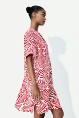 Vestido túnica a la rodilla en tejido liviano de viscosa con cuello mao y abertura en V. Modelo de corte holgado con hombros levemente caídos, mangas cortas y bajo recto con tajos laterales. Parte posterior algo más larga. Sin forrar. Estampado con motivos de hojas rojas.