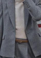 Abrigo gris con cuello de solapa, cierre frontal con botón, dos bolsillos laterales con solapa, un bolsillo de ribete en el pecho y puños abotonados.