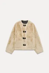 Chaqueta color beige de cuello redondo y manga larga con aberturas y botones. Tiene bolsillos de parche en la parte delantera y cierre frontal con botones metálicos.
