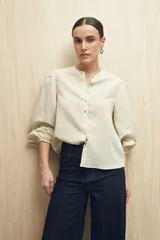 Camisa color crema a rayas verticales finas, de cuello mao, mangas 3/4 abullonadas con elástico en los puños y cierre frontal con botones de nácar.