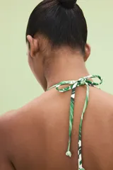 Top de bikini triangular blanco con estampado de hojas de palmera verdes y tirantes finos para atar al cuello y a la espalda.