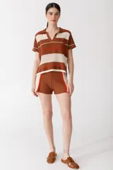 Remera polo tejida a rayas horizontales rojas y rosadas, con cuello clásico y bordado de ají verde.