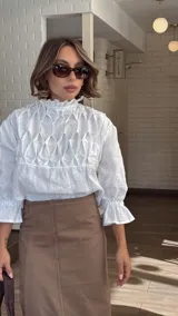 Blusa blanca de lino con cuello alto fruncido, mangas 3/4 con volados y detalle constructivo en el delantero con costuras a mano.