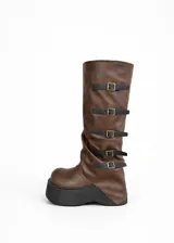Botas bucaneras de cuero vegano color marrón, con caña arrugada y plataforma gruesa negra. Presentan cinco tiras ajustables con hebillas doradas a lo largo de la caña.
