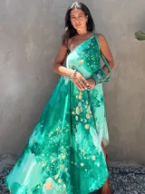 Vestido largo de tela fluida, color verde esmeralda con estampado abstracto en tonos turquesa y detalles dorados. Diseño asimétrico con un solo tirante tejido en el hombro.