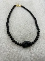 Collar corto de cuentas redondas de piedra de lava negra con una cuenta central de piedra negra pulida y cierre de gancho dorado.