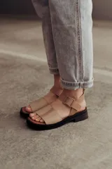 Sandalias bajas color arena, con tiras anchas de cuero y hebilla lateral.