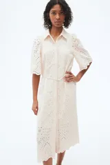 Vestido midi color beige con broderie, cuello camisero, botones ocultos, mangas abullonadas al codo, cinturón fino con borlas y ribete festoneado.