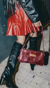 Cartera mini de cuero color bordó, con correa de mano y bolsillo interior con cierre.