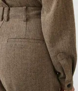 Pantalón de vestir de corte ancho, color marrón con textura tweed. Tiene cintura alta con trabillas, pliegues frontales, bolsillos laterales y un bolsillo trasero.