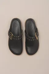 Sueco destalonado de cuero vacuno color negro, con hebilla ajustable dorada y detalles de tachas doradas.