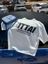 Remera color crema de corte recto y mangas cortas, con estampado en la espalda con el logo "ITTAI" en negro con líneas rojas, azules y blancas, y la leyenda "AN IBIZA PRODUCE. Ittai Stars Department Gallery - Ibiza Edition. If you're in Ibiza, 112 is not an option.".