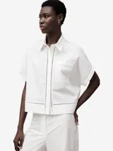 Camisa blanca de algodón con calados en el frente, ruedo y mangas. De corte recto, con cuello solapa, manga corta, botonadura frontal y bolsillo en el pecho.