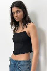 Top crop corsetero negro de popelín con escote recto, tirantes finos ajustables con lazada y bajo acabado con volante. Tiene forro interior a tono y cierre de cremallera en la espalda.
