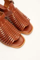 Sandalia de cuero color marrón con diseño de tiras entretejidas y hebilla lateral.