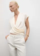 Blusa color crema de tejido fluido con diseño cruzado, cuello en V y sin mangas.