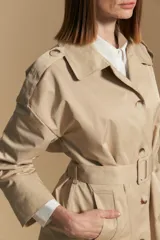 Trench color beige de corte clásico con cuello amplio, botones frontales, detalles en los hombros y mangas largas.
