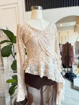 Blusa de encaje color rosa pálido con volados asimétricos y mangas largas acampanadas.