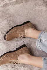 Mocasín de cuero negro con cordones y tachas metálicas en la puntera.