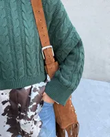 Bolso tipo bandolera de cuero color beige con flecos y tachas plateadas.