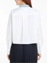 Camisa blanca de algodón orgánico, nailon y elastano, con cuello de rayas celestes y cierre con botones dorados. Tiene corte boxy, manga larga, bolsillo de parche en el pecho y logo de Tommy Hilfiger bordado en el puño.