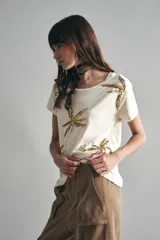 Remera de mangas cortas color crudo, de calce relajado y escote redondo. El frente se encuentra bordado con un diseño de palmeras en lentejuelas y canutillos.