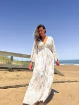 Vestido largo color crudo con estampado dorado, escote en V y mangas acampanadas.