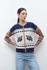 Chaqueta de tejido punto con cierre frontal, cuello redondo y manga larga. Presenta un diseño jacquard en tres colores: azul marino, beige y marrón camel. El cuerpo principal es beige con motivos de rosas azules y patrones geométricos en azul marino. Los hombros y mangas son de color marrón camel con patrones geométricos en azul marino. El cuello y el elástico inferior son de color azul marino.
