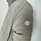 Campera puffer color beige con cierre frontal y cuello alto. Diseño acolchado con bolsillos laterales.