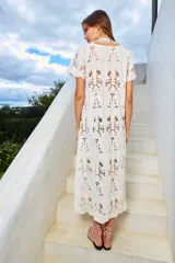 Vestido largo color crudo, con cuello redondo y manga corta. Confeccionado en tela de encaje de algodón con diseño floral y tajo lateral.