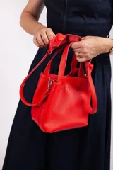 Mini bolsa de cuero graneado roja, con asa doble y correa larga desmontable, detalles de volado en el diseño.