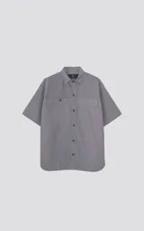 Camisa gris de manga corta confeccionada en poplin 100% algodón, con silueta oversize y dos bolsillos delanteros, uno con solapa y otro con ojal y botón.