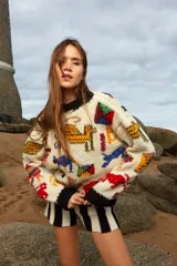 Sweater tejido a mano de lana color crudo con cuello redondo y puños negros. Presenta bordados con motivos abstractos en colores.