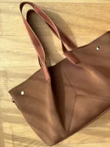 Bolso negro tipo tote de neopreno con bolsillo interno de red, sobre haciendo juego y gancho para sujetarlo.