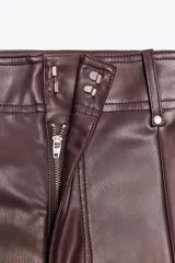 Pantalón marrón de tiro alto con efecto cuero, bolsillos de parche en la parte trasera y costuras marcadas en la parte delantera. Cierre frontal con cremallera y gancho metálico.