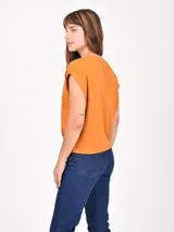Remera de manga corta, color naranja quemado, con cuello redondo y mangas caídas que simulan un efecto de hombro doblado.