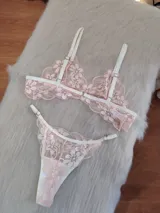 Conjunto de lencería de dos piezas, compuesto por un corpiño tipo bralette y una bombacha tipo colaless, ambos confeccionados en encaje floral color coral/rosado pálido con detalles y elásticos en blanco.