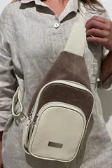 Mochila bandolera de cuero color marrón chocolate y detalles en color crema. Tiene dos bolsillos con cierre y correa regulable.