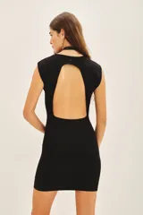 Vestido corto negro de punto, sin mangas, con cuello alto y espalda descubierta.