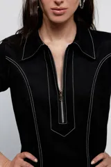 Vestido corto negro de jean, con cuello camisero, medio cierre delantero y pespuntes blancos en contraste.