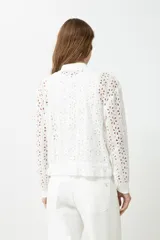 Campera blanca de broderie con cierre frontal, cuello redondo y mangas largas.